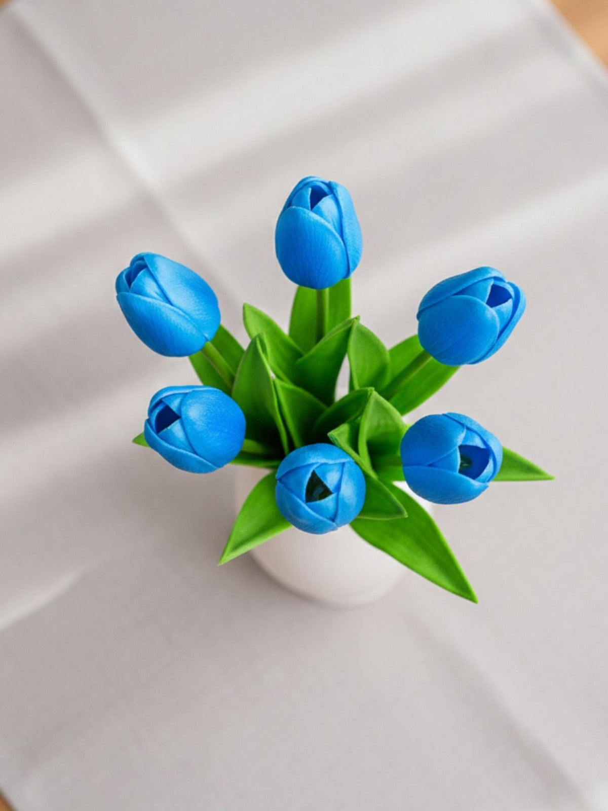 Blue tulips in a white vase on a white fabric background