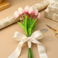 Bouquet of baby pink tulips with a white ribbon on a beige surface with decorative items.