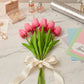 Bouquet of pink tulips with a white ribbon on a marble surface with jewelry and cards.