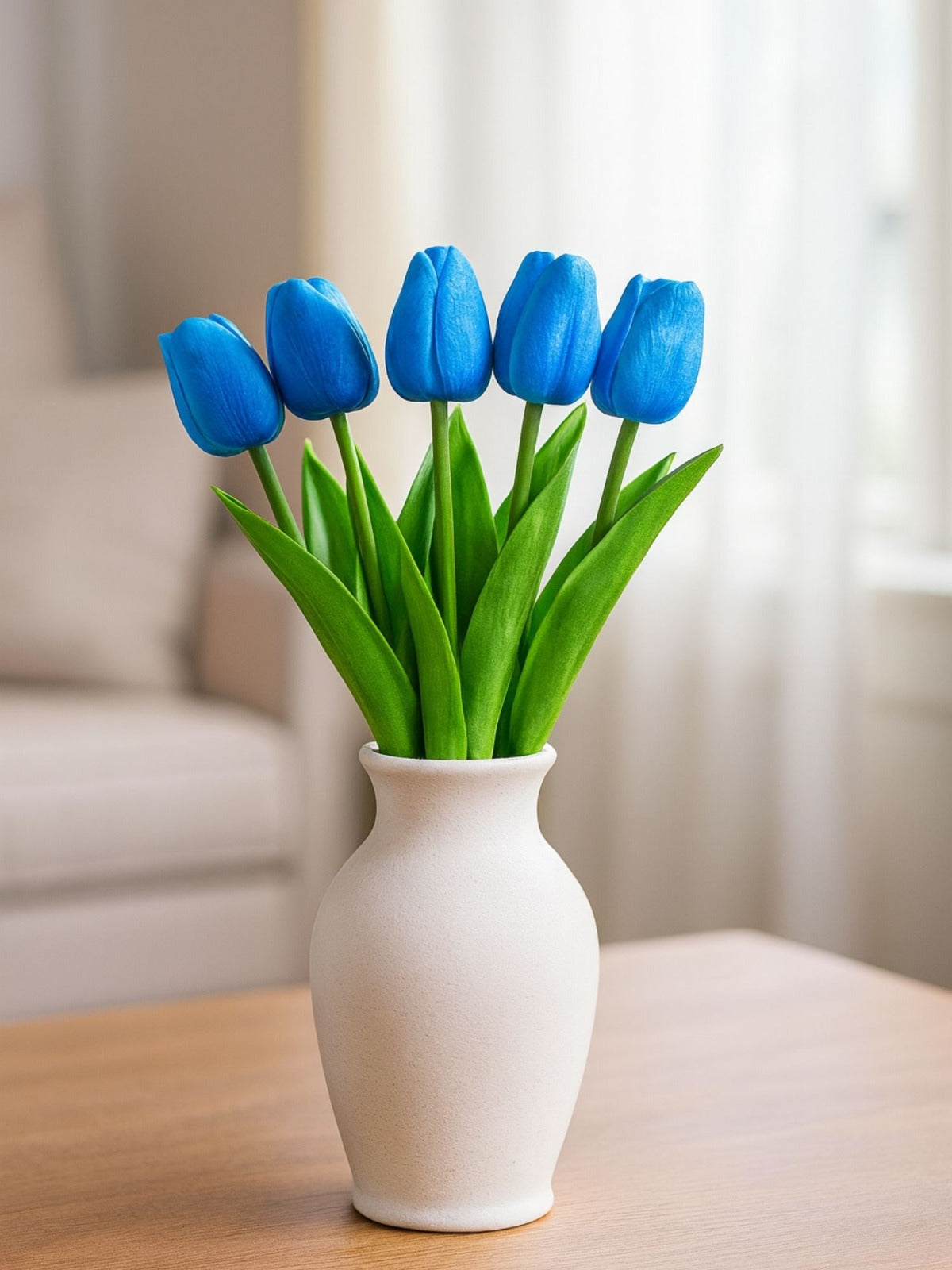 White vase with blue tulips on a wooden surface