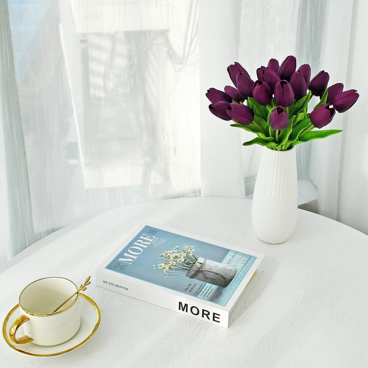Vase of purple tulips on a table with a book and cup.