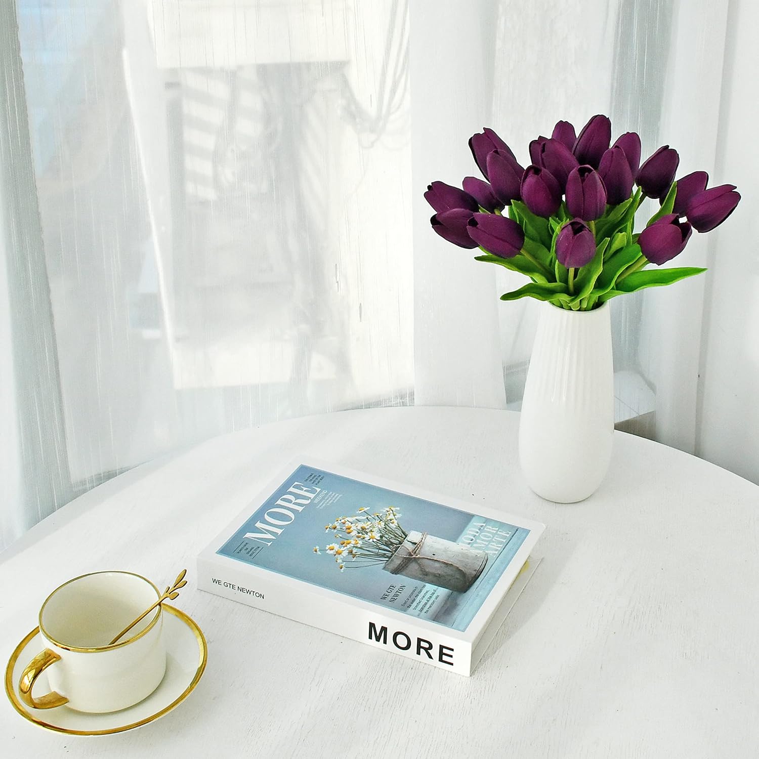 Vase of purple tulips on a table with a book and cup.
